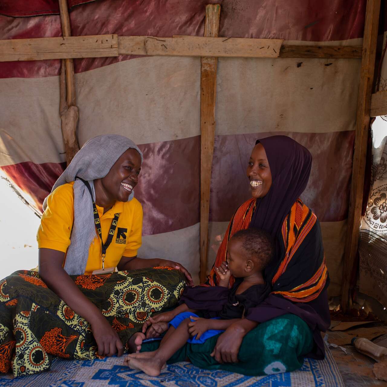 국제구조위원회 고객인 한 엄마가 아기를 안고 스탭과 함께 환하게 웃고 있습니다.
